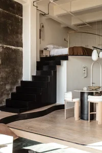 A modern industrial bedroom featuring a metal floating bed on a black staircase against a textured black wall, with a white s
