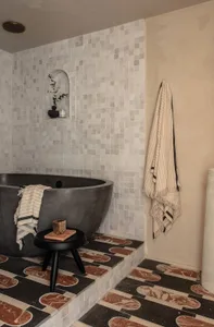 A minimalist bathroom featuring a concrete bathtub, patterned marble tiles, and a hanging towel.