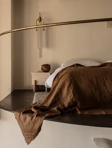 Minimalist bedroom with brown linen bedding, brass light fixture, and concrete surfaces