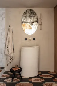 A modern bathroom featuring a concrete sink, round mirror, and patterned floor tiles.