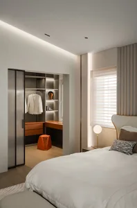 A modern minimalist bedroom featuring a white bed with a white blanket, a white headboard, and an orange stool.