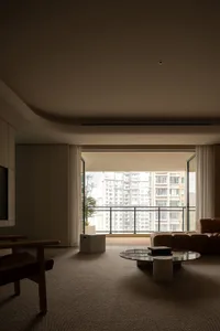 A modern minimalist living room featuring a textured rug, a round glass coffee table, and a plush brown sofa with a potted pl