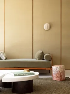 Minimalist living room featuring textured wall paneling, a sleek daybed with green upholstery, and a unique side table with a