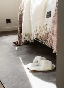 A cozy setting featuring a pair of fluffy white slippers, a textured blanket, and a soft rug in a comfortable home environmen