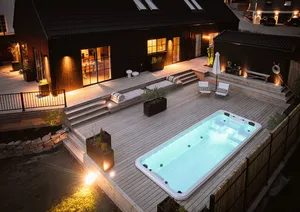 Modern residential backyard featuring a wooden terrace, concrete swimming pool, and stylish outdoor furniture, illuminated at