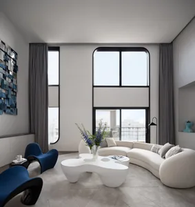 Modern living room with large windows featuring a white, curved sofa, blue armchairs, and a unique white coffee table with fl