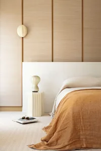 A minimalist bedroom features a textured wall background, a bed with a plain white headboard, and a bedside table with a uniq