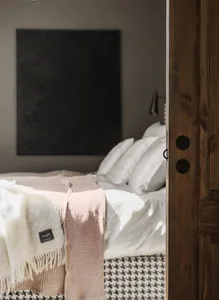 A minimalist bedroom with a wooden door, white bedding, and soft textiles.
