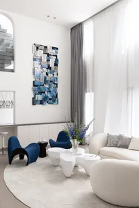 A modern living room featuring abstract art on the wall, a white sofa, blue armchairs, and a round rug.
