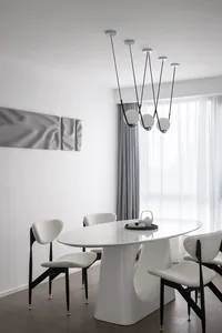 Modern dining room featuring a sleek, white oval table with four chairs, minimalistic design, and hanging pendant lights.