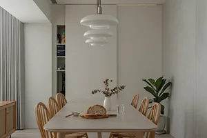 A minimalist dining room with concrete tables and chairs, featuring a modern pendant light fixture and a plant in a white vas