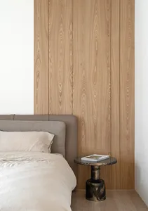Minimalist bedroom with a bed, wooden wall paneling, and a bedside table with a book.