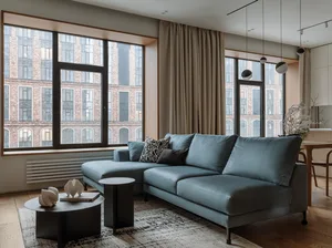 A modern living room featuring a blue sofa with patterned and dark pillows, black coffee tables, and a large window with beig