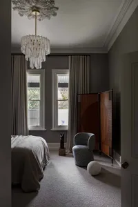 A minimalist bedroom with grey walls, a grey bed, and a grey carpet, featuring a stylish chandelier and decorative screens.