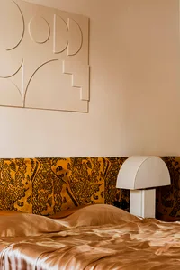 A minimalist bedroom with a yellow-patterned headboard and a gold-colored bedspread.