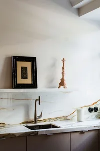 A minimalist kitchen with a white marble countertop featuring a stainless steel faucet and a white ceramic mug.