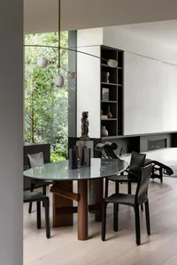 Modern dining room featuring a wooden table with a glass top, surrounded by black leather chairs and a brass pendant light.