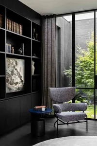 A modern library space featuring black wooden shelves, a cozy armchair, and a small circular table with a vase and a cup.
