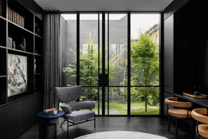 A modern living room featuring floor-to-ceiling glass walls with a view of greenery outside.