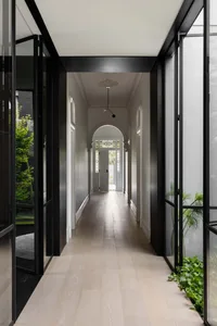 A modern minimalist hallway with light-colored wooden floors, clear glass panels, and white walls.