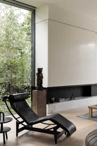 A modern minimalist living room with a leather chaise lounge, large window, and a minimalist fireplace.