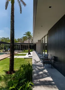 A modern minimalist residence with a concrete outdoor living area featuring a lounge chair, pool, and greenery.