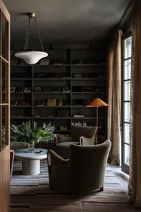 Industrial living room featuring plush green armchairs, glass lampshade, bookshelves, and green plants