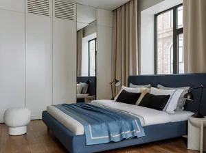 Modern minimalist bedroom with a blue upholstered bed, white linens, and black lamps.