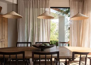 A minimalist dining room with wooden furniture, three wicker pendant lights, and long curtains.