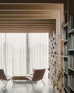 A modern minimalist library with wooden bookshelves and white curtains. Modern lounge chairs are positioned facing a large wi
