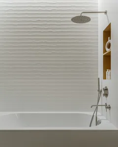 A modern, minimalist bathroom with textured white tiles covering the walls and ceiling, and a sleek, clean bathtub design.