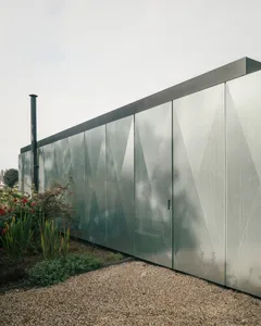 A modern exterior house with a metallic facade, featuring geometric patterns and a chimney.