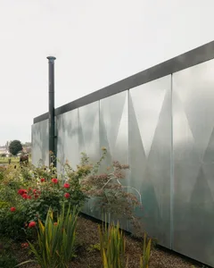 A modern exterior featuring a metal panel wall with a diamond pattern and a chimney.