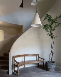 A modern minimalist living room with a wooden bench, a potted plant, and a spiral staircase.