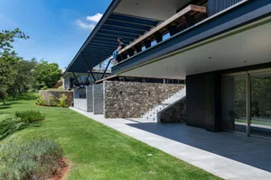 A modern residential building with a concrete and stone exterior, featuring a large balcony and a landscaped garden.