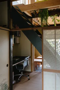 A minimalist home office with a wood desk and chair, surrounded by greenery.