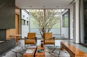 A minimalist living room featuring two brown leather armchairs, a marble side table, and a wooden bench.