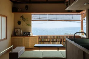 A minimalist living room with sea view, showcasing wicker furniture, woven rugs, and a bookshelf filled with books.