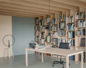 A modern home office featuring a wooden desk, bookshelves filled with books, and a black office chair.