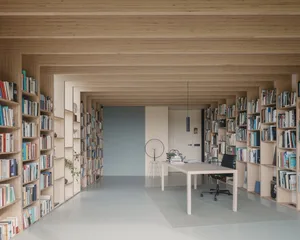 A modern home office with a library filled with books and a minimalist table and chair setup.