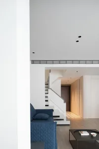 A modern living room featuring white marble stairs, a blue sofa, and a black coffee table.