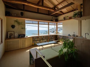 A modern living room featuring wooden furniture, glass panels, and a carpeted floor, with a view of the ocean through the lar