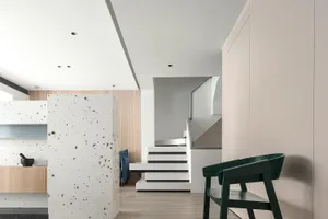 A modern residential interior featuring a white speckled wall, white and black stairs, and a green chair in a simple, clean s