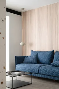 A blue sofa in a minimalist living room featuring a modern design with wooden walls and a pendant light fixture.