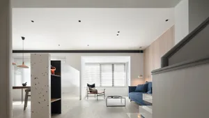 A minimalistic living room featuring a blue sofa and a coffee table on a terrazzo floor, with a black ceiling track.