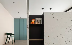 Modern minimalist interior featuring a concrete wall with a black shelving unit displaying a lamp and a magazine.