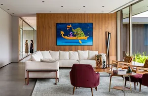 A modern living room with a white couch, wooden walls, and a colorful painting of an elephant on a boat.
