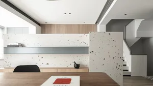 A modern office space featuring a desk with a book and a red book cover, a grey shelf on a wall with books, and stairs in the