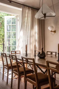 A modern dining room with wooden table and chairs, fabric cushions, and large windows