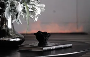 A minimalist interior decor setup featuring a metallic vase with a flower arrangement and a black book with a black ceramic o